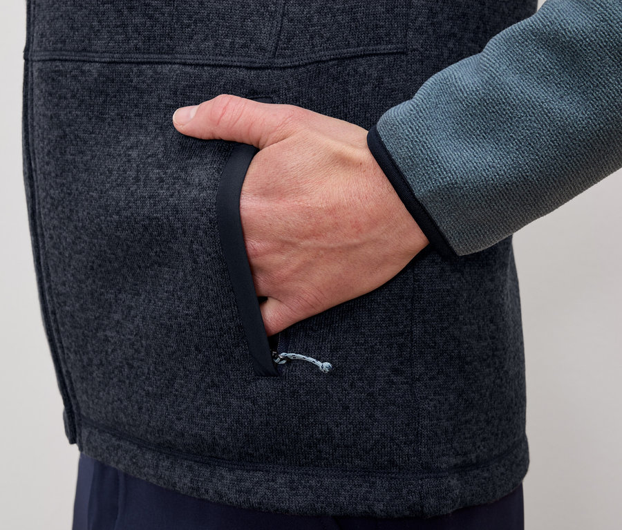 Un homme met sa main dans la poche d'une veste en polaire gris-bleu.