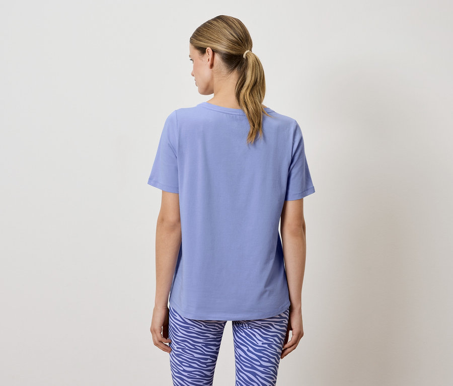 Une femme, dos à la caméra, porte un t-shirt bleu et un legging à motifs animaliers.