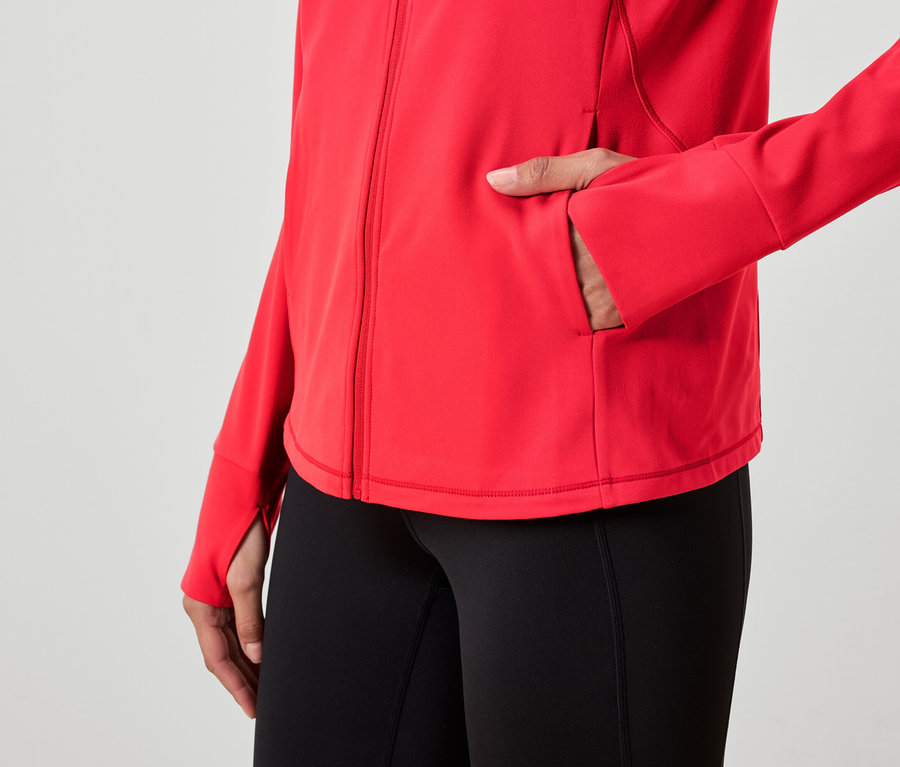Une femme a une main dans la poche d'une veste rouge et porte un legging noir.