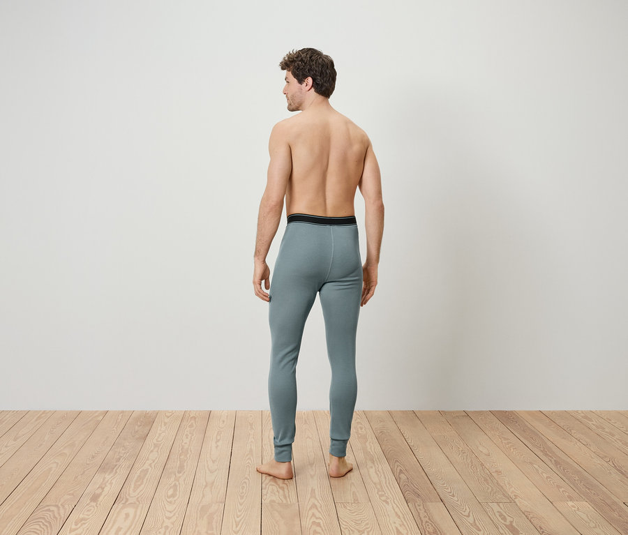 Un homme dos à la caméra porte des sous-vêtements thermiques gris.