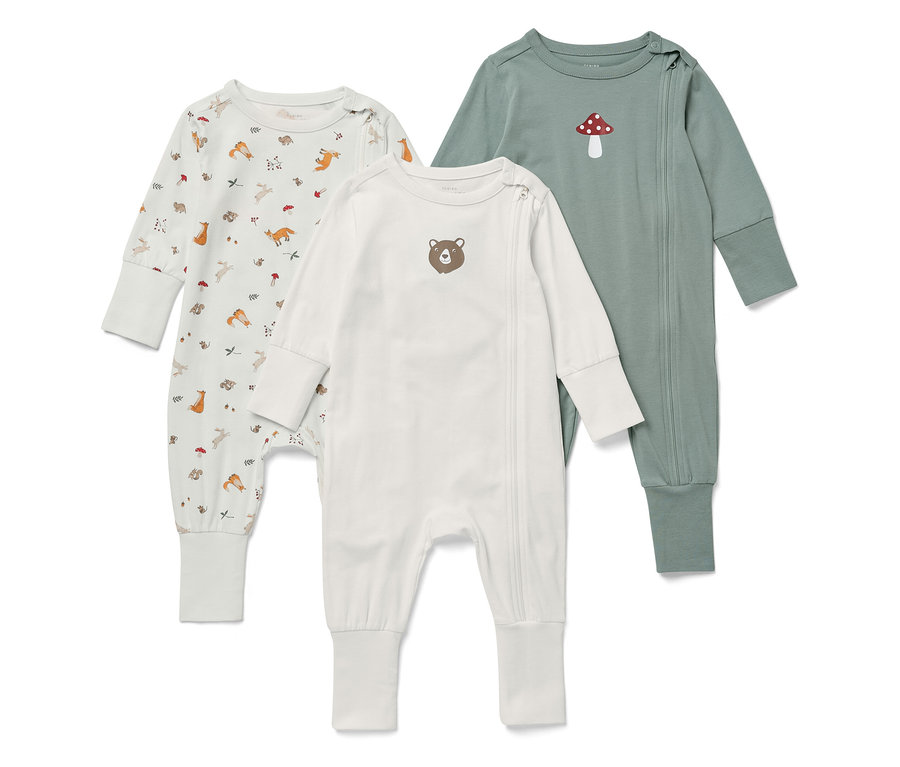 Trois pyjamas pour bébés à manches longues sont placés côte à côte. L'un est blanc avec des motifs d'animaux, l'autre est blanc avec un ours et le troisième est vert avec un champignon.