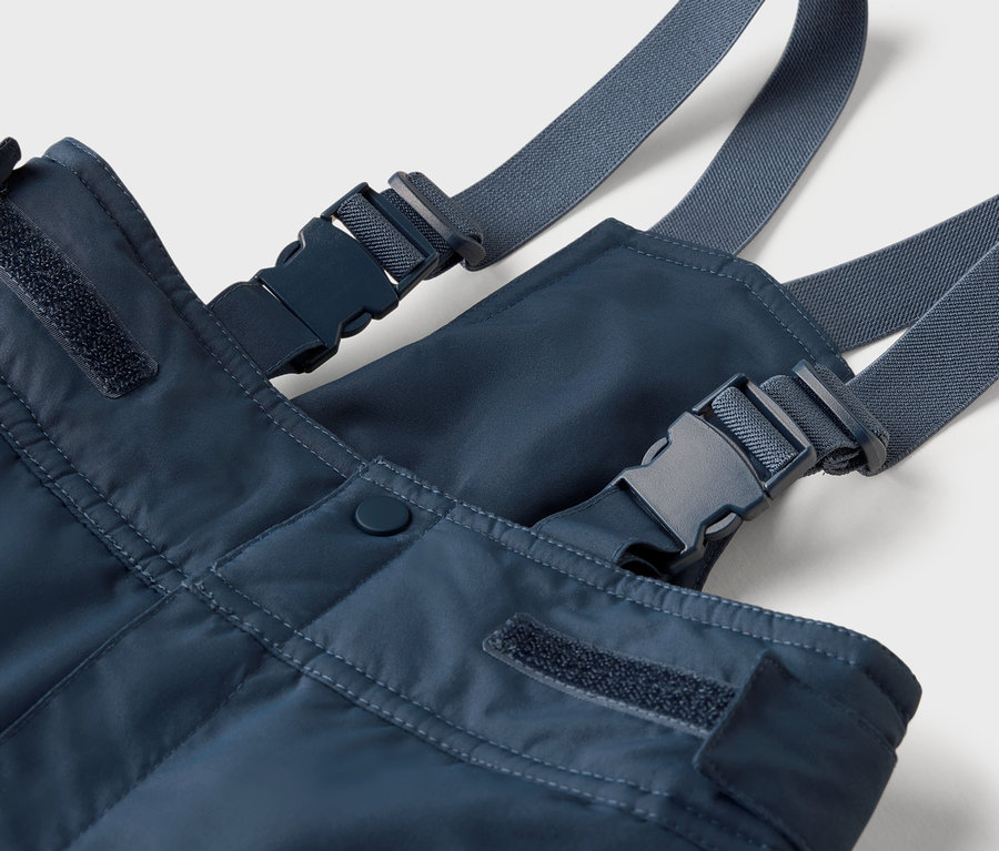 Gros plan sur une salopette bleue avec des bretelles grises et des boucles en plastique.