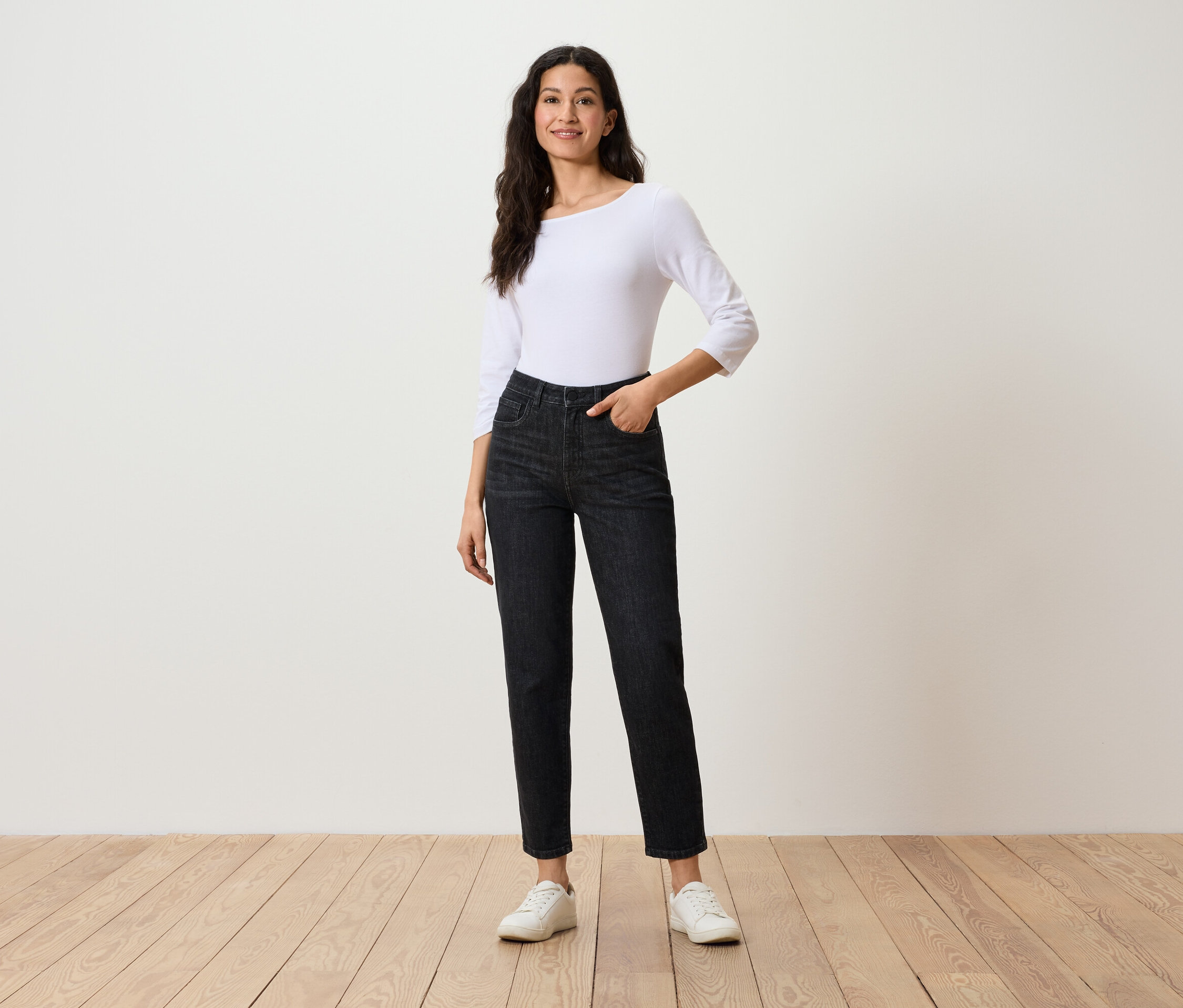 Femme posant en jean noir, haut blanc à manches trois-quarts et baskets blanches.