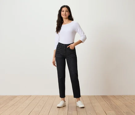 Femme posant en jean noir, haut blanc à manches trois-quarts et baskets blanches.