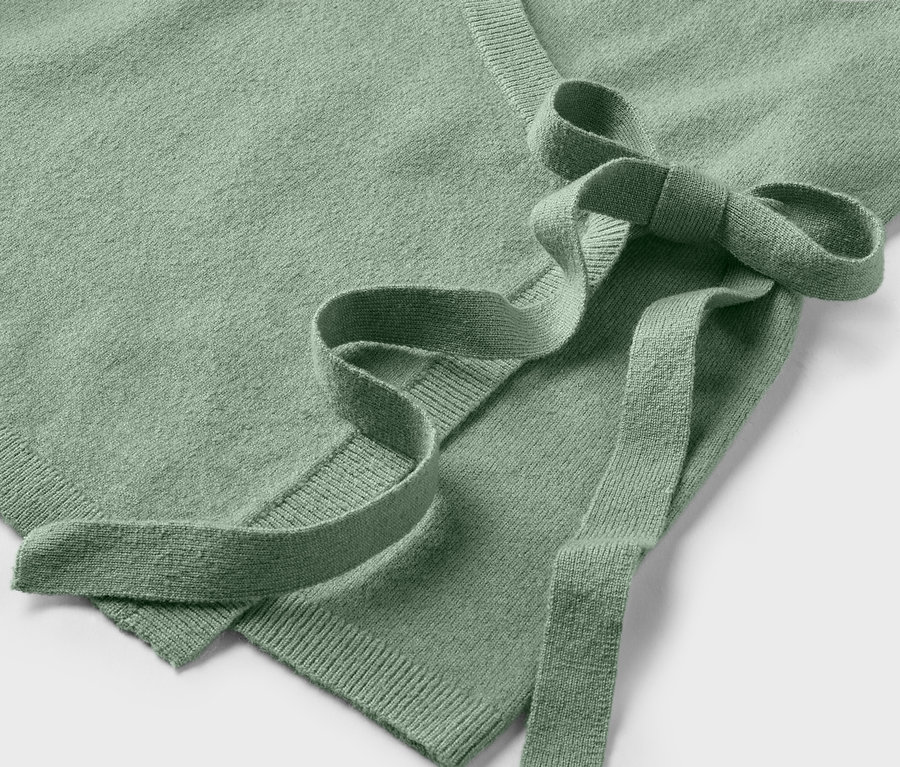 Gros plan sur un pull cache-cœur vert clair avec une ceinture à nouer.