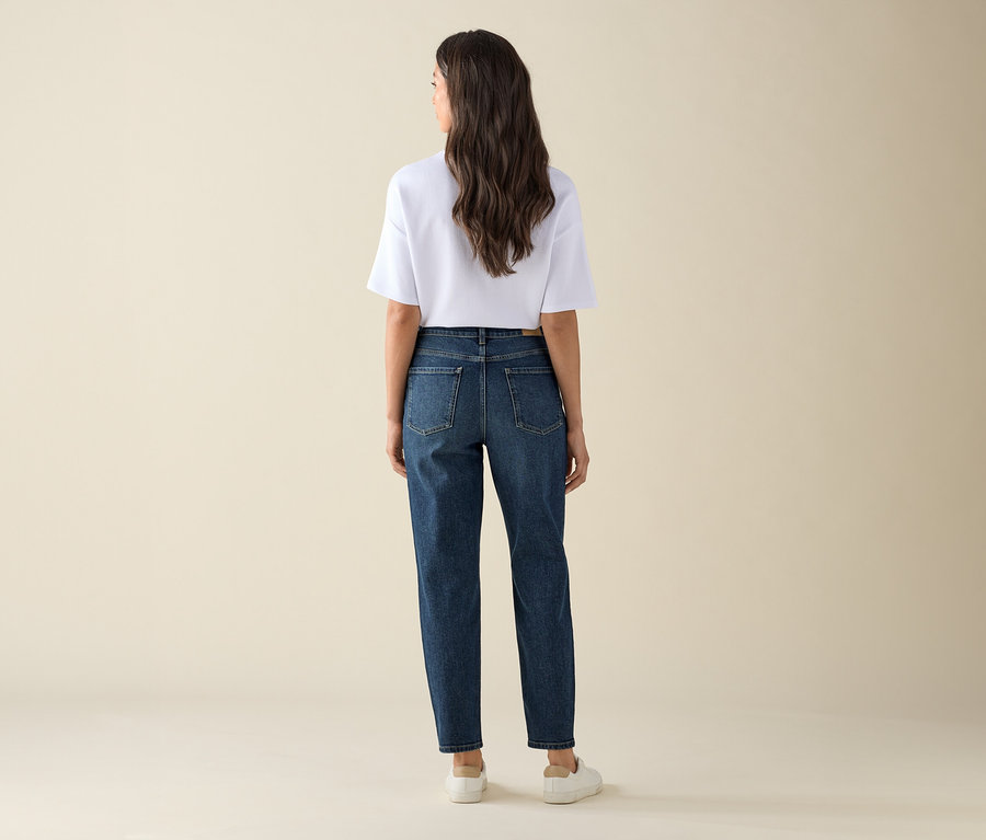 Une femme, vue de dos, porte un Mom Jeans – Coupe « Nyla », bleu foncé et un t-shirt blanc.