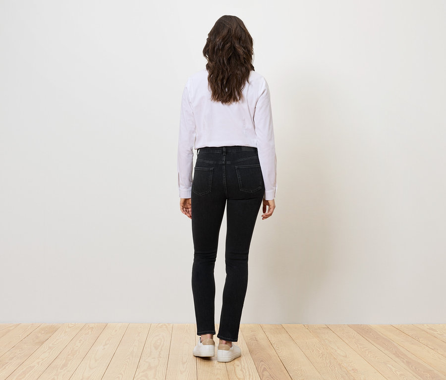 Femme vue de dos portant un jean noir, une chemise blanche et des baskets blanches.