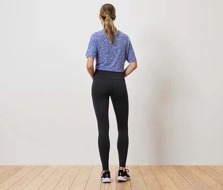 Une femme portant des leggings noirs et un haut bleu et blanc, dos à la caméra.