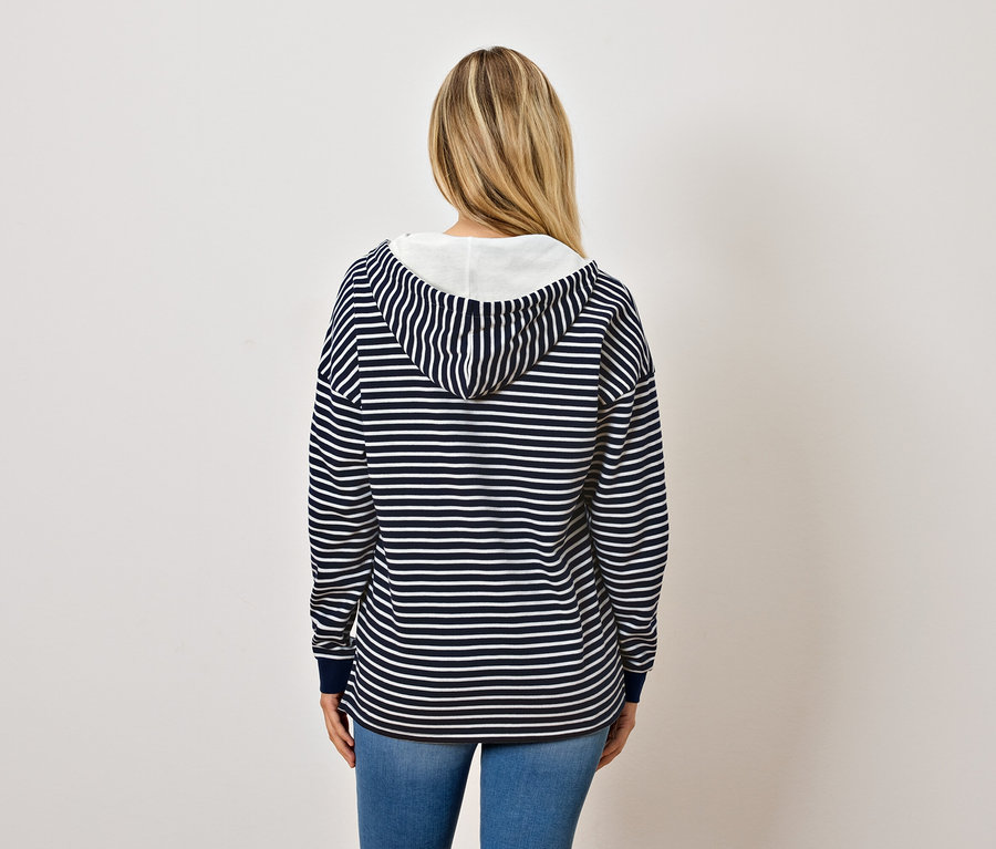 De dos, une femme aux cheveux blonds porte un sweat à capuche rayé bleu et blanc et un jean.
