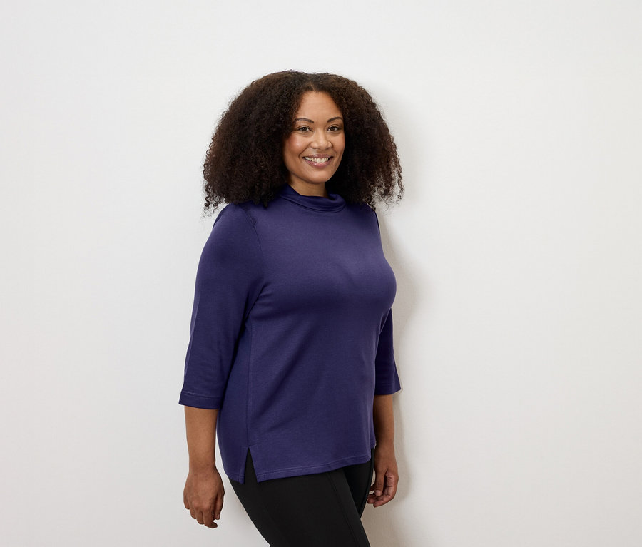 Femme portant un sweatshirt avec col montant aubergine et des leggings épais avec liseré.