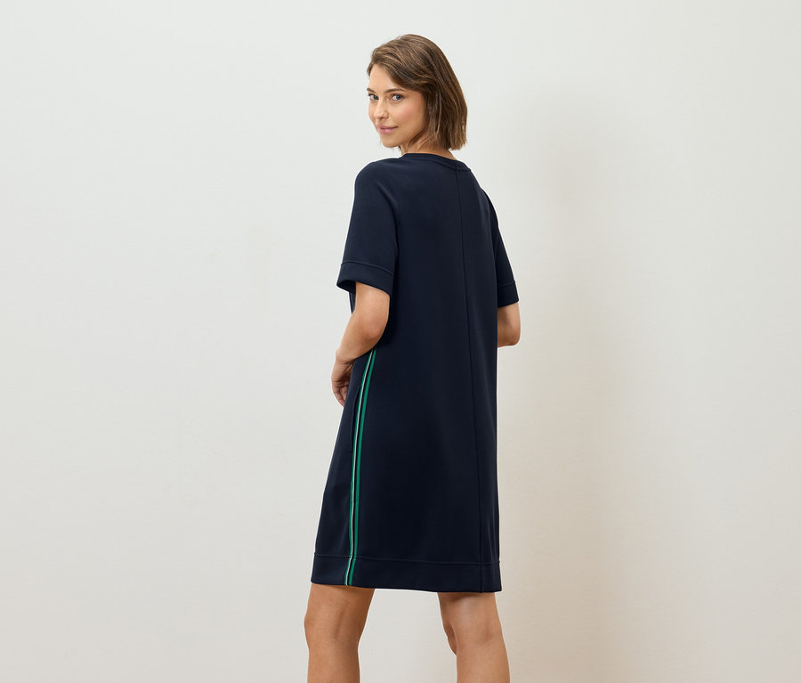 Une femme regarde par-dessus son épaule et porte une robe t-shirt bleu marine avec une bande verte.
