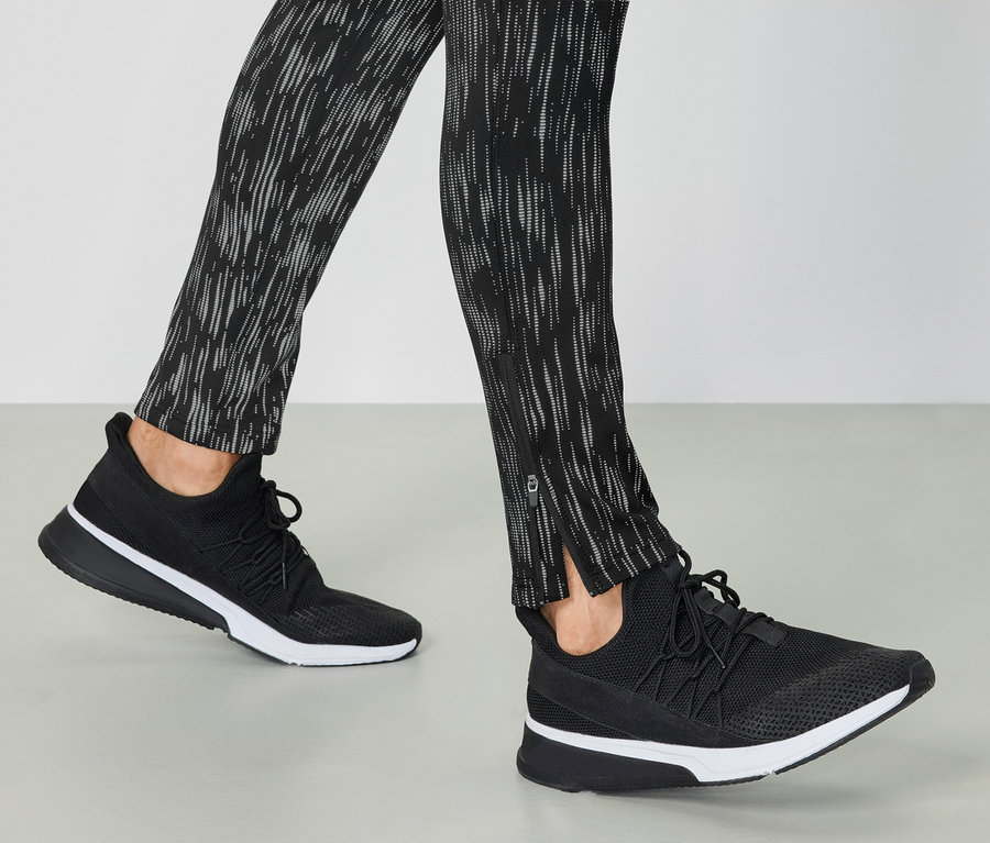 Jambes portant des chaussures de sport noires et des leggings à motifs.