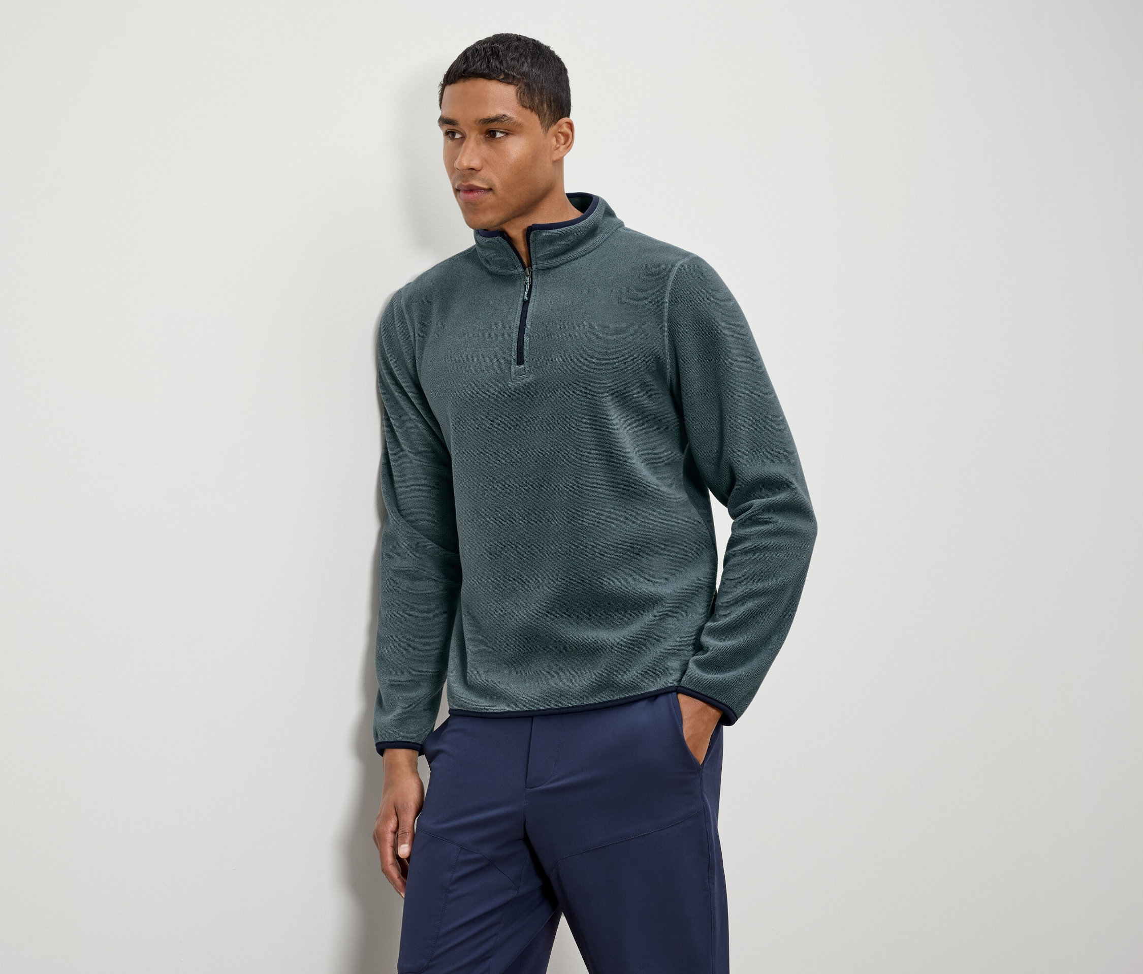 Un homme porte un pull en polaire vert avec un pantalon bleu marine.