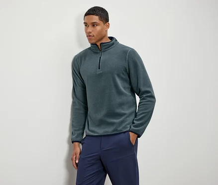 Un homme porte un pull en polaire vert avec un pantalon bleu marine.