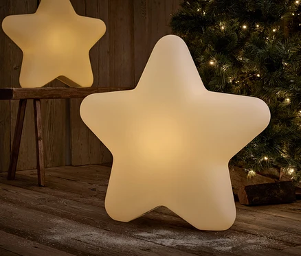 Deux décorations lumineuses en forme d'étoile sur un plancher en bois devant un arbre de Noël.