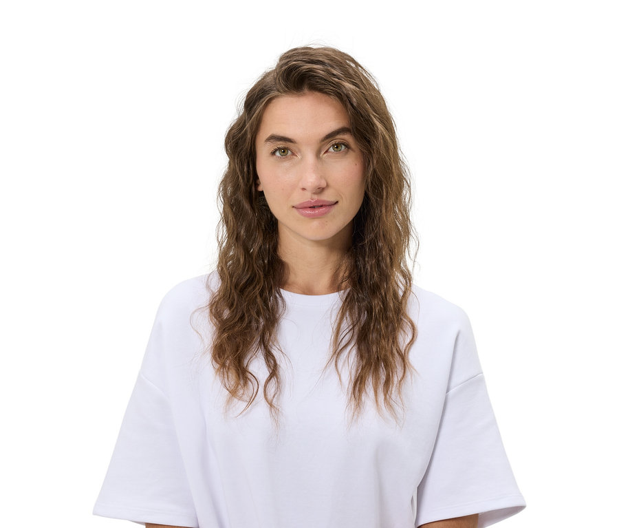 Portrait d'une femme aux cheveux bruns ondulés portant un t-shirt blanc sur fond blanc.