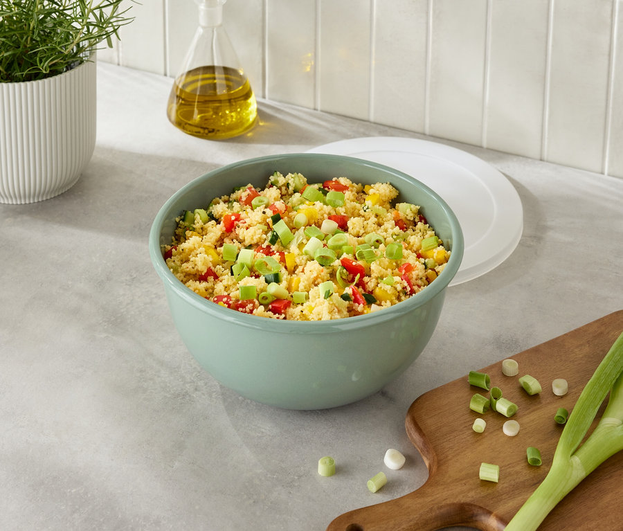 Un bol vert de couscous et de légumes à côté d'oignons sur une planche à découper.