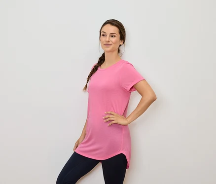 Femme aux cheveux bruns tressés posant dans un t-shirt rose et un legging bleu marine.