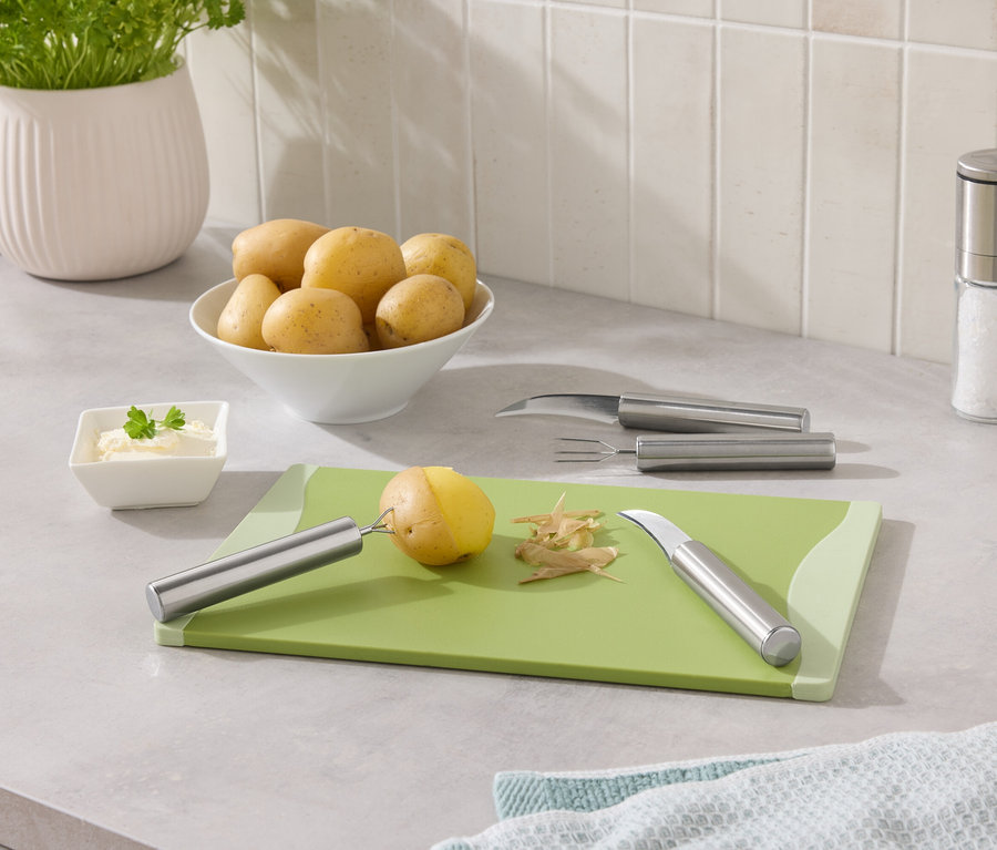 Des pommes de terre dans un bol et une pomme de terre en train d'être pelée sur une planche à découper verte.