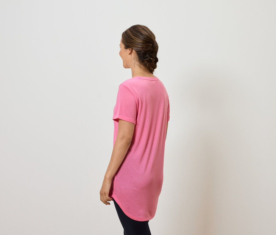 Une femme, vue de dos, porte un t-shirt rose et un pantalon foncé.