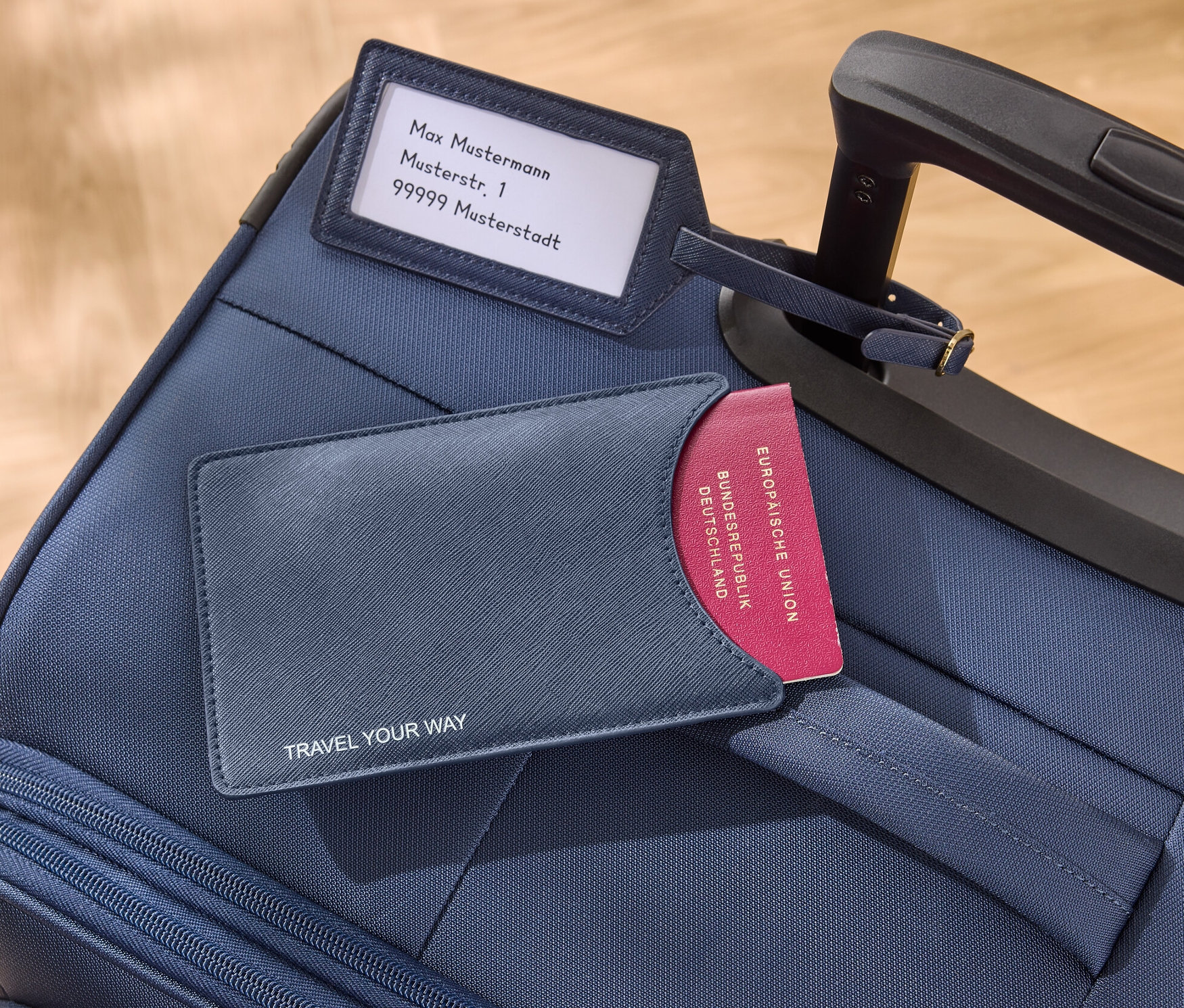 Sur une valise bleue reposent une pochette pour passeport bleue et une étiquette à bagage.