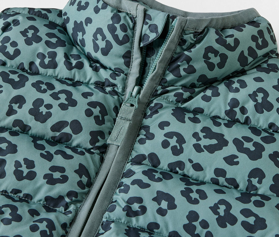 Gros plan sur une veste sans manches matelassée pour enfant avec un motif animalier et une fermeture éclair.