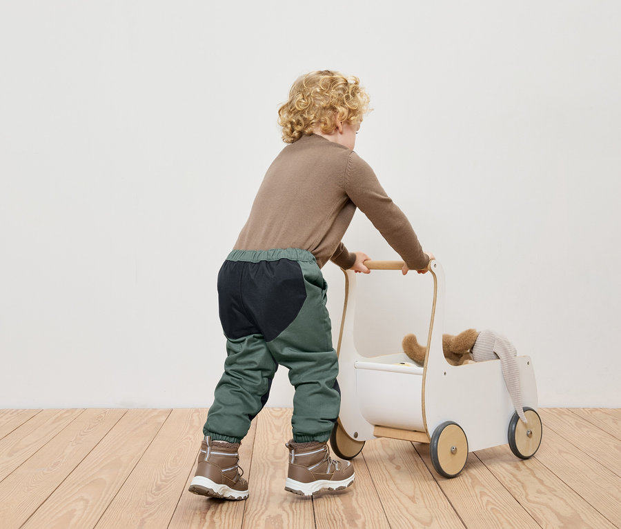 Un garçon pousse un chariot à jouets blanc sur un plancher en bois.