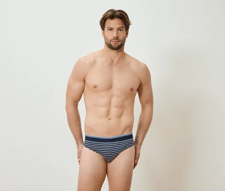 Homme torse nu en slip rayé debout devant un mur blanc.