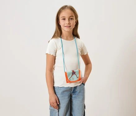 Fille portant un t-shirt clair et un jean, avec un petit sac à bandoulière avec un singe dessus.
