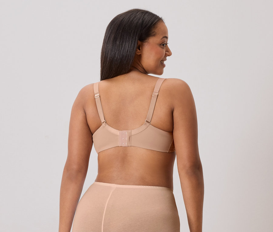 Vue de dos d'une femme aux longs cheveux foncés portant un soutien-gorge couleur chair et des sous-vêtements assortis.