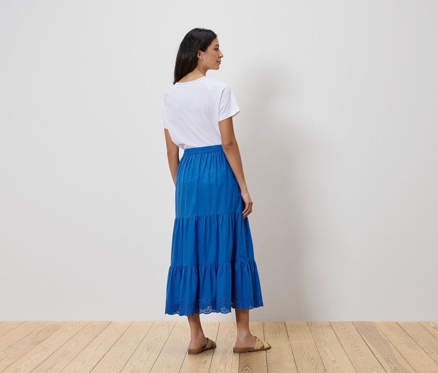 Une femme se tient dos à la caméra, portant un t-shirt blanc et une jupe bleue à volants.