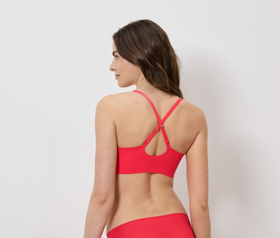 Femme vue de dos, portant un soutien-gorge rouge à bretelles croisées et un slip assorti sur fond blanc.