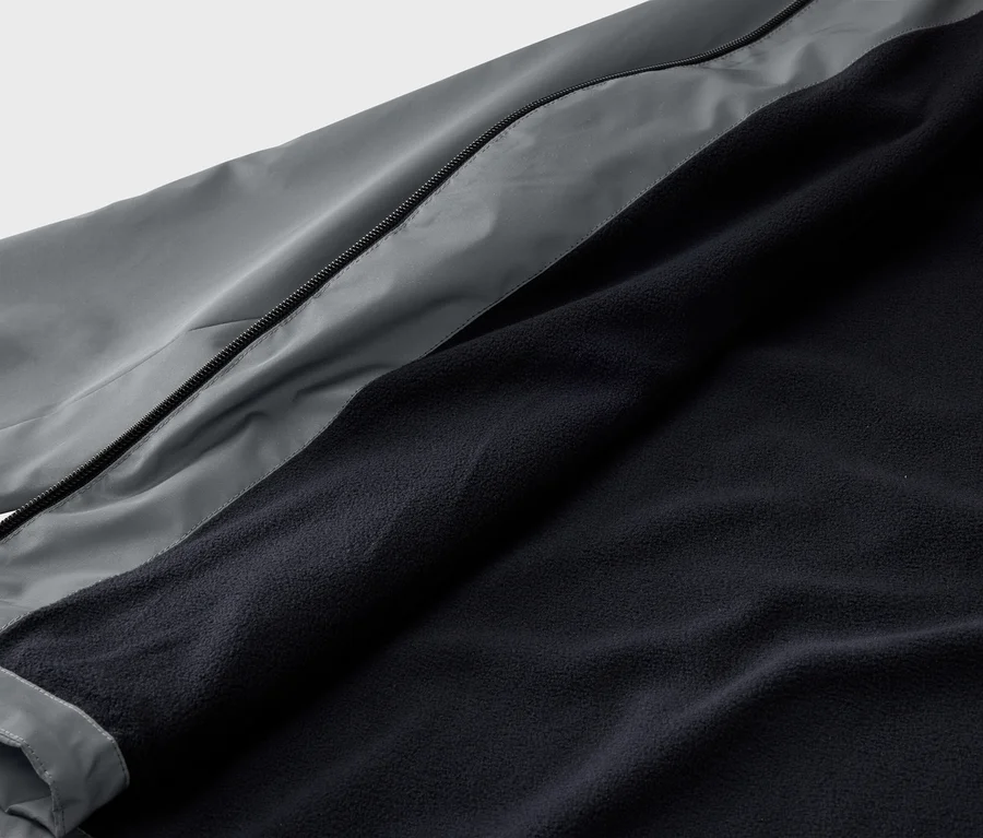 Gros plan d'une veste ouverte présentant un extérieur gris et une doublure en polaire bleu marine.