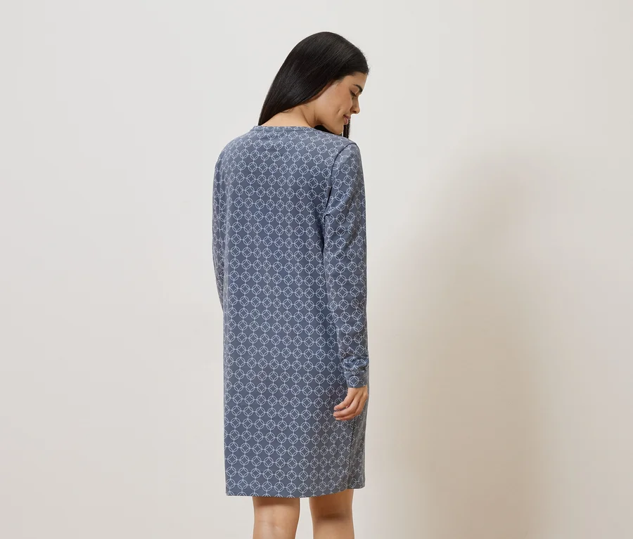 Une femme aux longs cheveux foncés porte une robe bleue à motifs et à manches longues.
