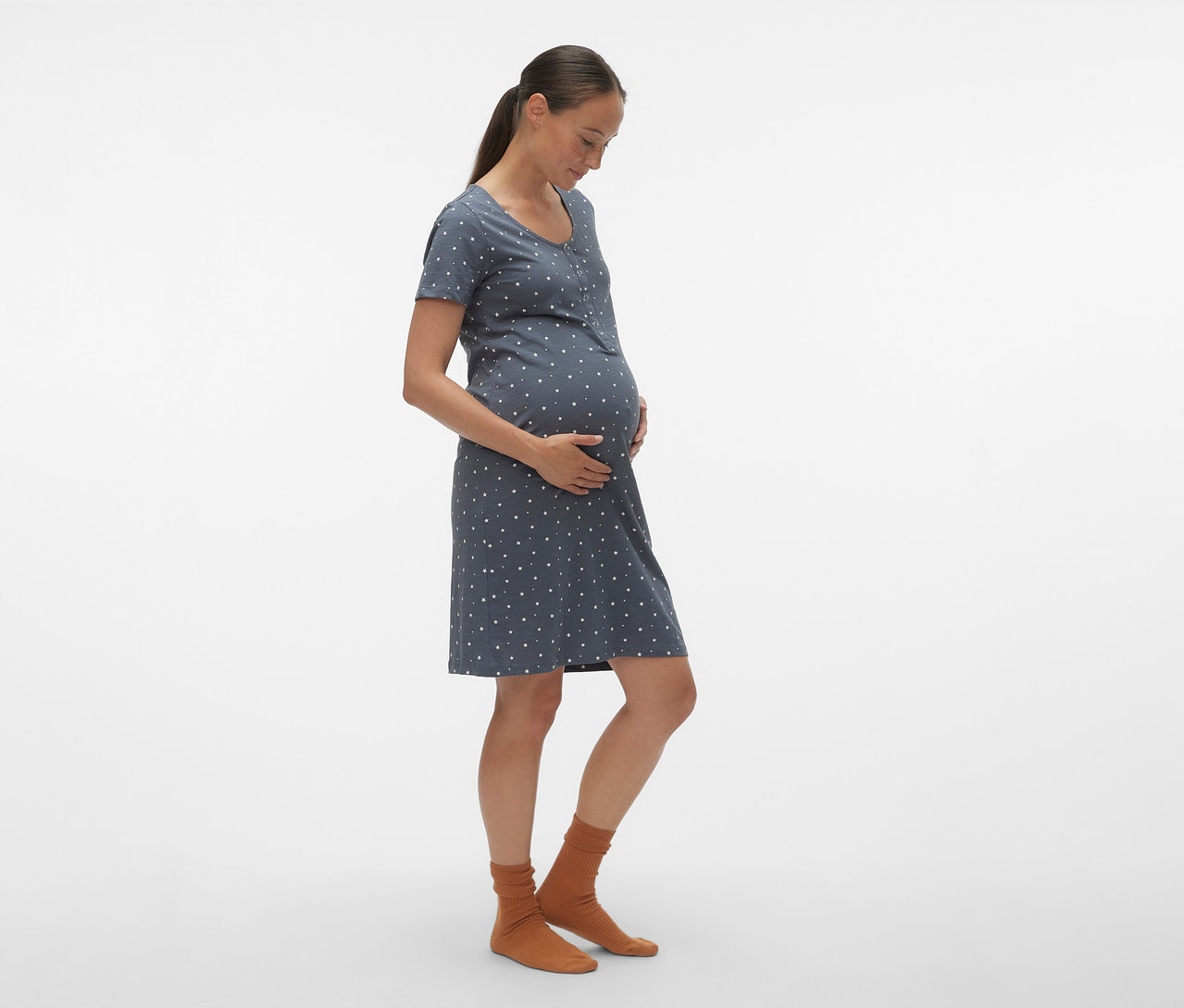 Une femme enceinte de profil porte une chemise de nuit bleue à pois blancs MAMALICIOUS «
MLMIRA » et des chaussettes marron.