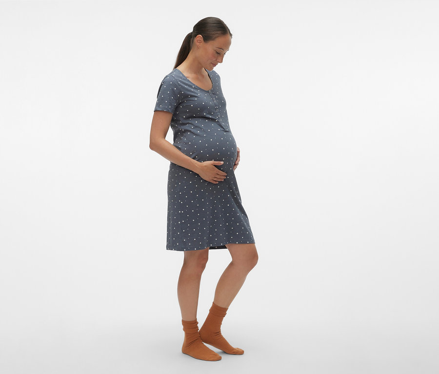 Une femme enceinte de profil porte une chemise de nuit bleue à pois blancs MAMALICIOUS «
MLMIRA » et des chaussettes marron.