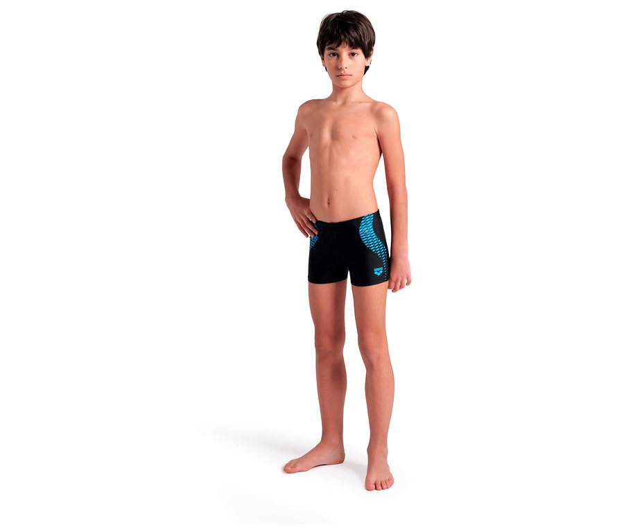 Un garçon aux cheveux foncés pose en maillot de bain noir avec un motif bleu.