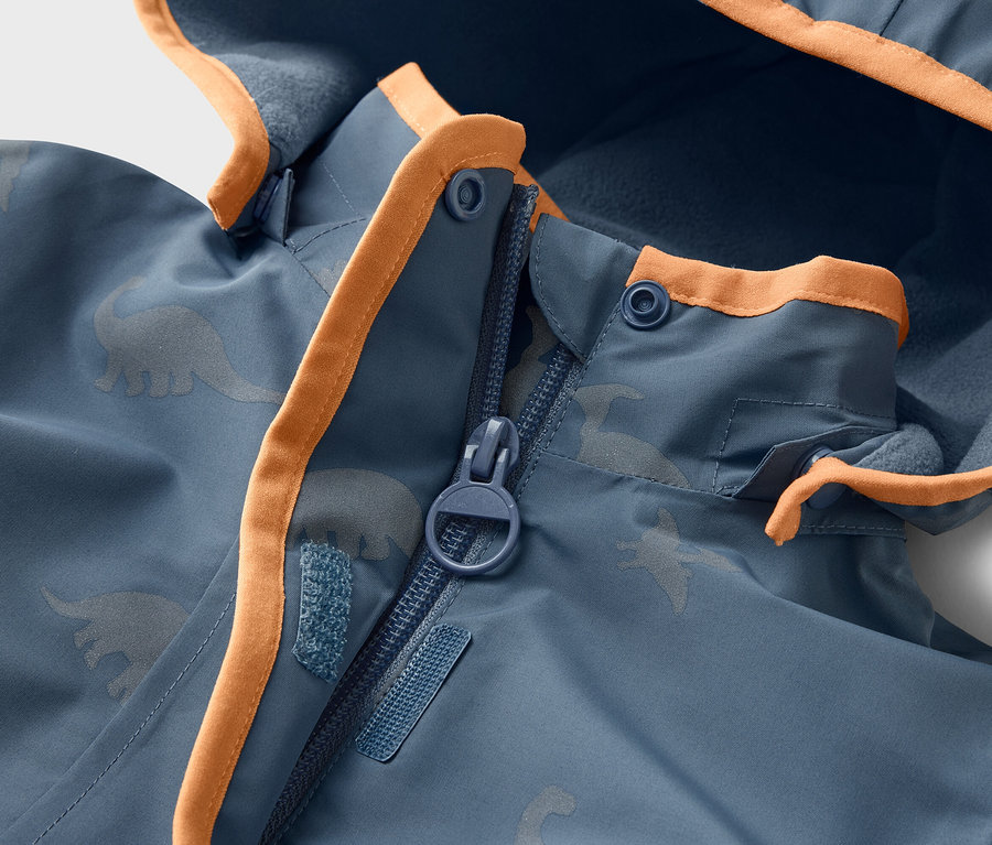 Gros plan sur une veste bleue à motif de dinosaures avec des détails orange et une fermeture éclair.