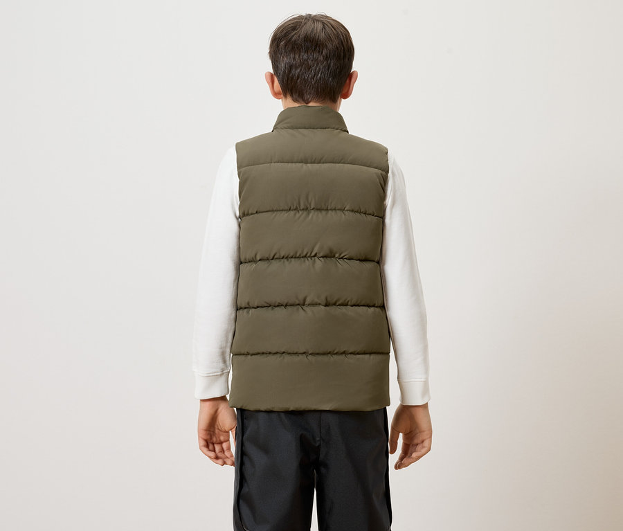 Vue arrière d'un enfant portant un pull blanc, un pantalon noir et un gilet matelassé vert olive sur fond blanc.