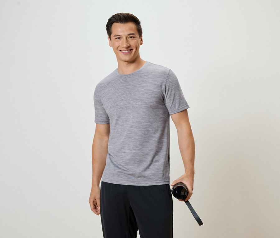 Un homme portant un t-shirt gris et un pantalon noir tient une bouteille d'eau.