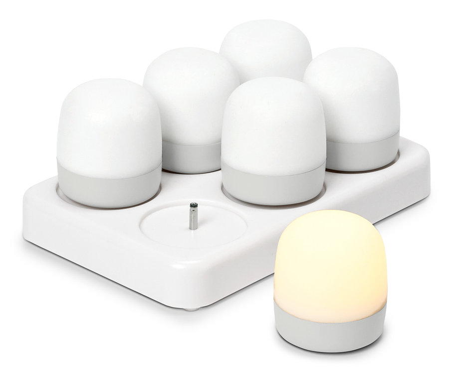 Cinq veilleuses blanches et rondes dans une station de charge, une autre veilleuse allumée se trouve à côté.