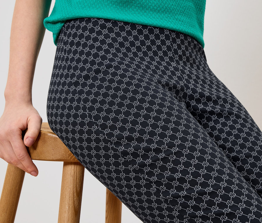 Une personne est assise sur un tabouret en bois et porte un pantalon avec un motif graphique.
