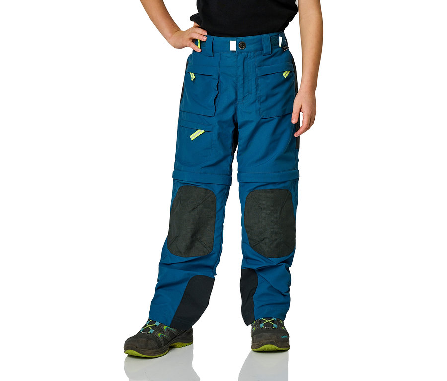 Enfant portant un pantalon d'extérieur bleu avec des patchs aux genoux et des chaussures de randonnée.