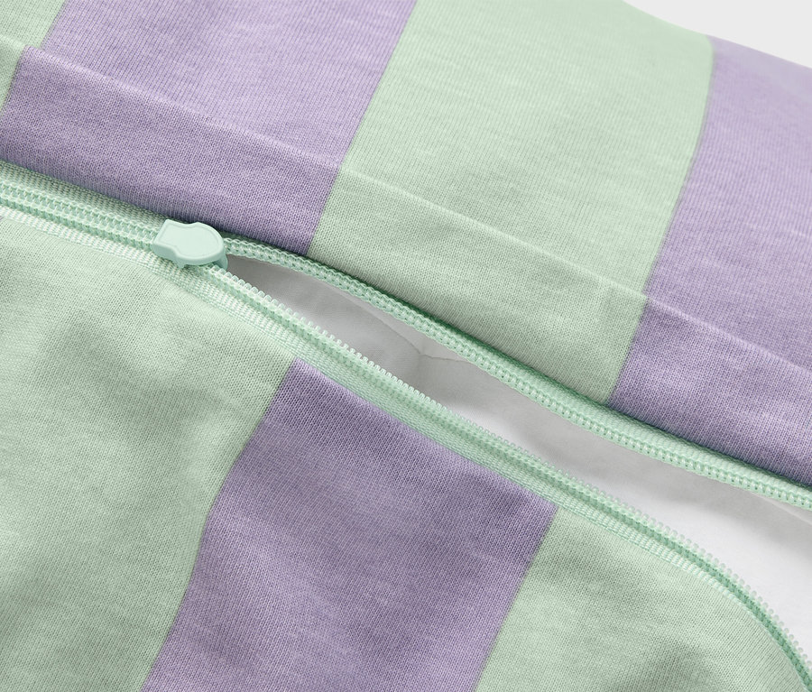 Gros plan d'une taie d'oreiller partiellement ouverte avec une fermeture éclair verte et un motif rayé violet et vert.
