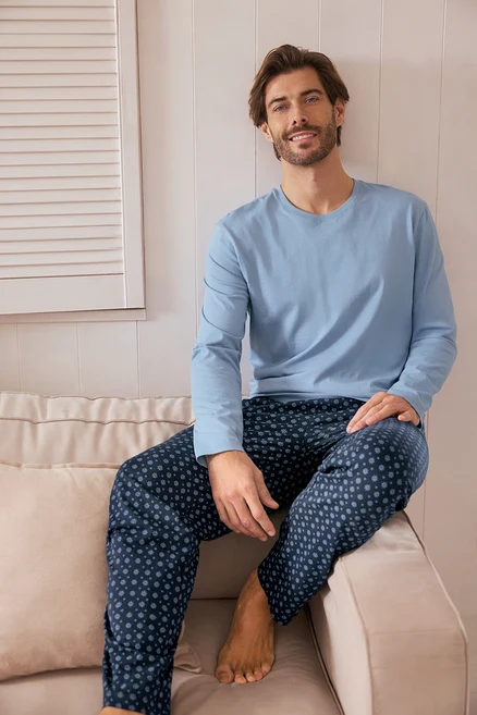 Un homme est assis sur un canapé, portant un pull bleu clair et un pantalon bleu marine à pois.
