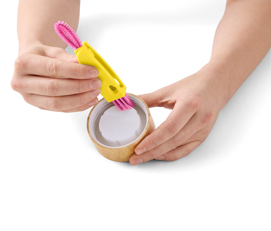 Une personne nettoie une tasse en bambou avec une brosse de nettoyage jaune à poils roses.