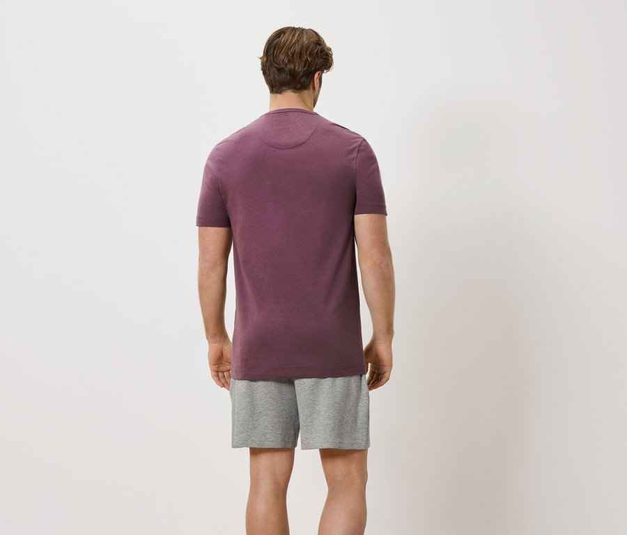 Homme vu de dos portant un t-shirt bordeaux et un short gris sur fond blanc.