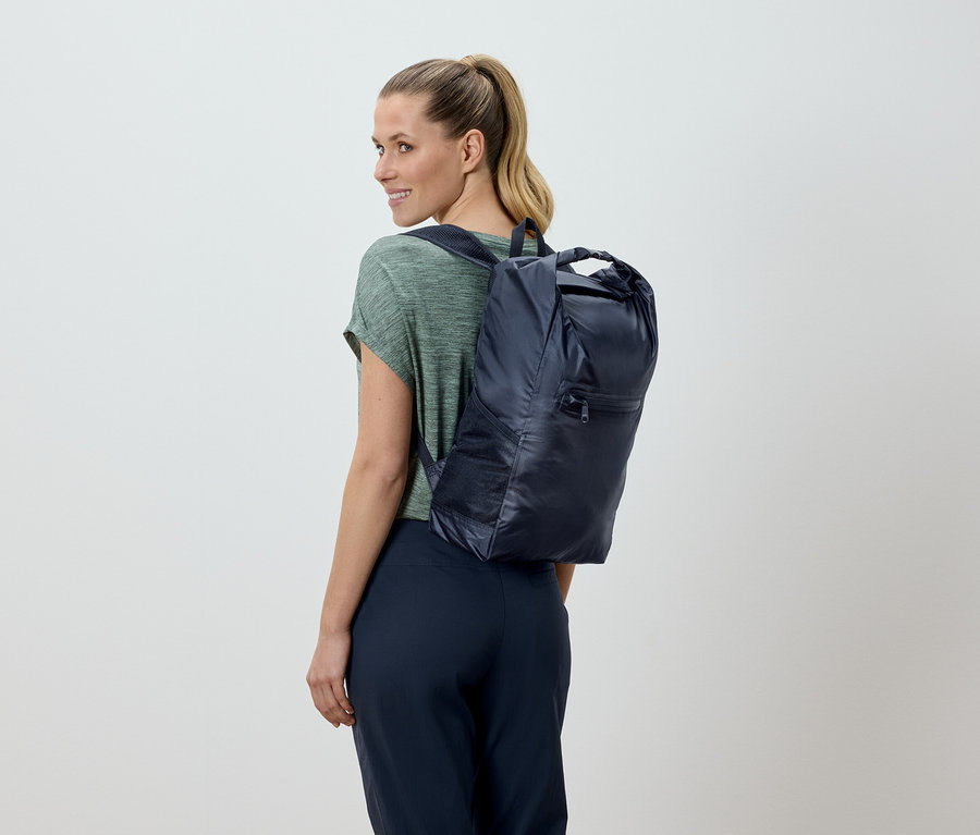 Femme blonde, vue de dos, portant un sac à dos bleu marine.