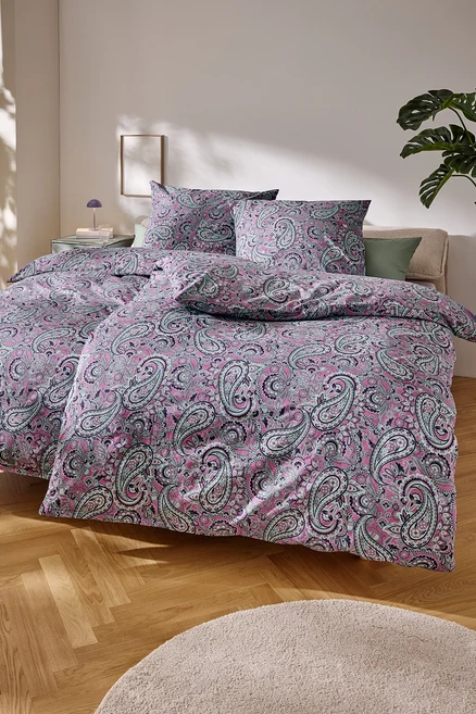 Gros plan d'un lit avec du linge de lit rose à motif cachemire.