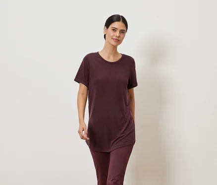 Femme portant un t-shirt bordeaux et un legging sur fond neutre.